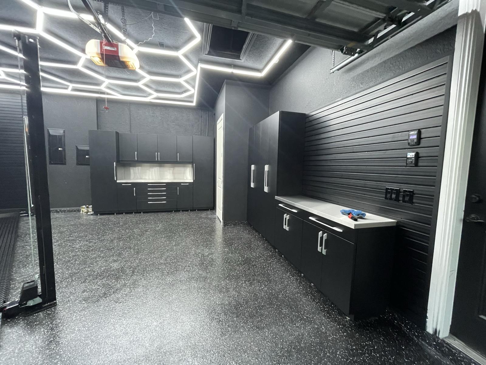 A finished home garage with a STAK lift post, epoxy floor, hex ceiling lighting and fitted cabinets